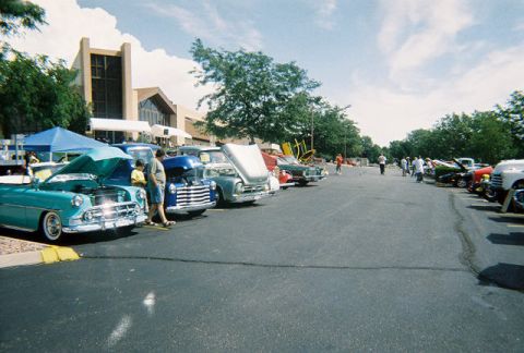 1972 Ford Ranchero - A line of classic cars are displayed at an outdoor car show, with one turquoise vehicle prominently featured with its hood up.