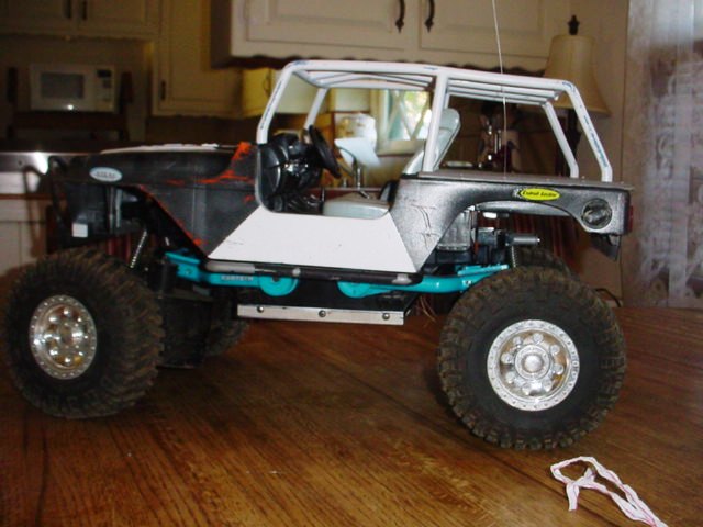 RC crawler vehicle with large tires and a roll cage, sitting on a wooden surface