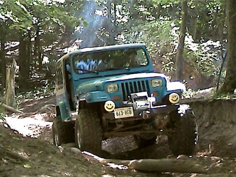 1977 Ford F-150 - A blue Jeep Wrangler navigates a muddy, wooded trail with a winch mounted on the front bumper.