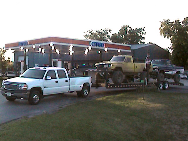 Yellow pickup truck on trailer in front of Citgo, with white GMC and blue Ford trucks nearby