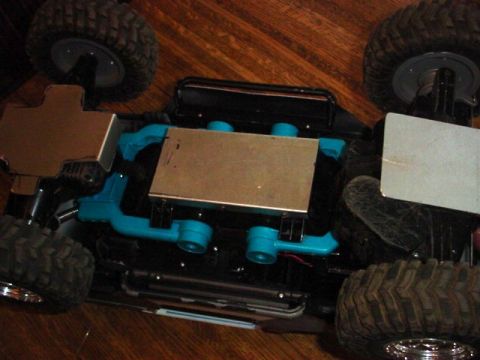 1988 Ford Bronco - Underside view of an RC crawler chassis, blue suspension parts and protective metal plating.