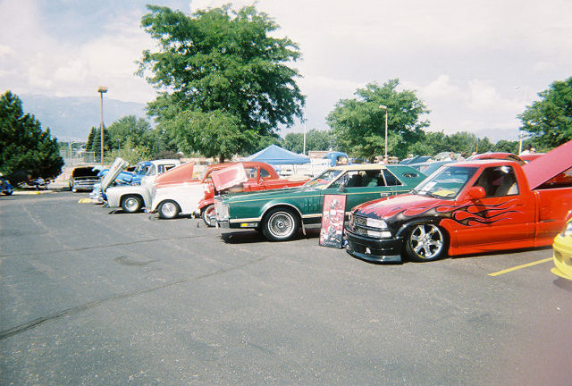 Several cars and trucks parked in a lot, some with hoods up. A red truck with flames is in the foreground
