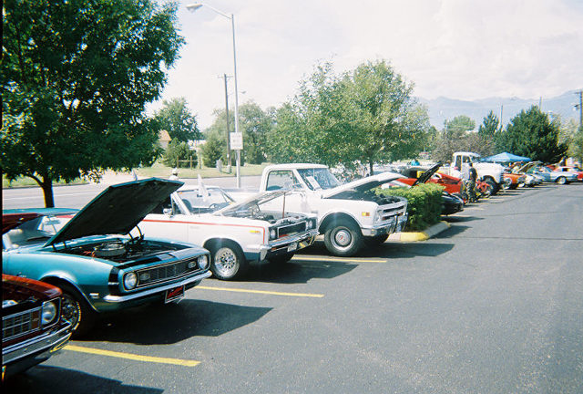 Line of cars parked at a show, hoods up. Blue 1967-1969 Camaro in foreground