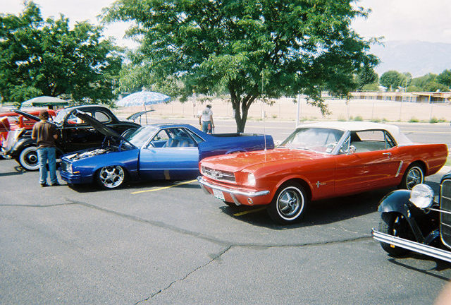 Several cars parked in a lot, including a red convertible and a blue coupe with its hood up