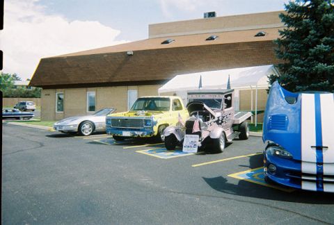 1972 Ford Ranchero - Several vehicles are parked in a lot outside a building, possibly at a car show event.