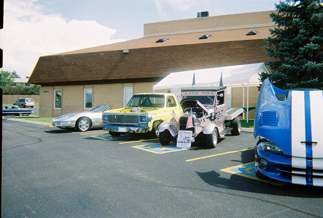 Silver sports car, yellow pickup truck, and a blue sports car with hood open parked at a car show