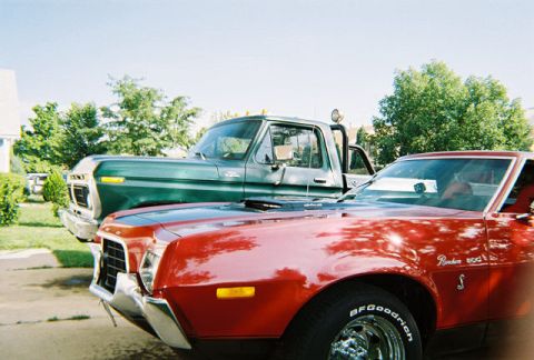 1972 Ford Ranchero - A red coupe and a green pickup truck are parked side-by-side on a sunny day.