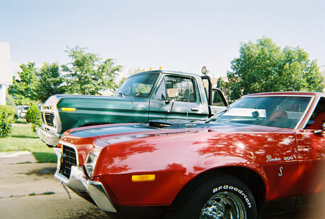 Red Ford Ranchero 500 in a driveway with a green Ford pickup parked behind it