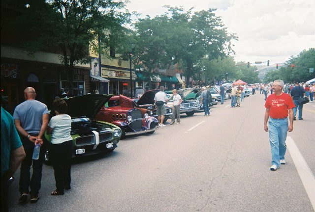Green car with hood open, red hot rod, and other vehicles lined up on a street