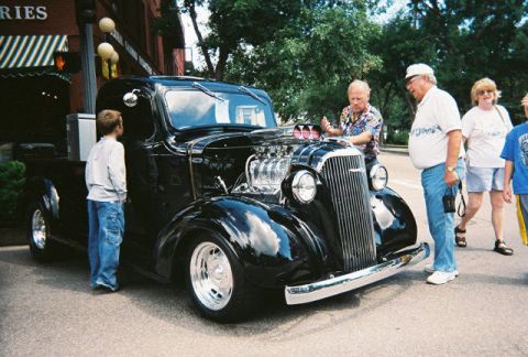 1972 Ford Ranchero - A black hot rod pickup truck with its hood open, revealing a powerful engine, draws attention at a car show.