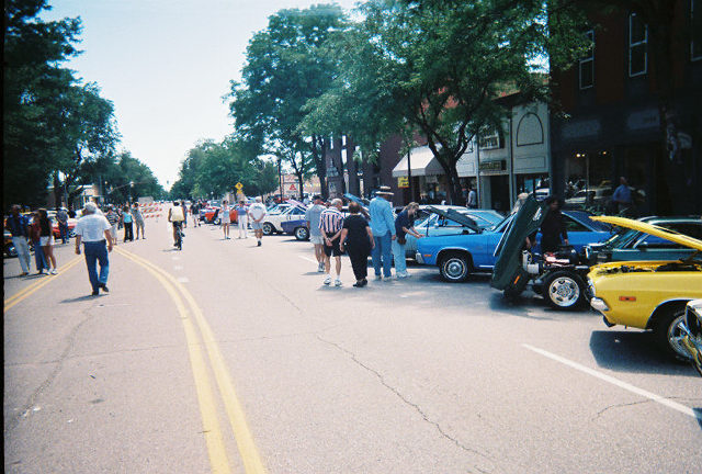 Street scene with people walking around parked cars, some with hoods open