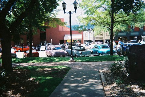 1972 Ford Ranchero - Several vintage vehicles are on display at an outdoor event, including a pink car and a gray pickup truck.