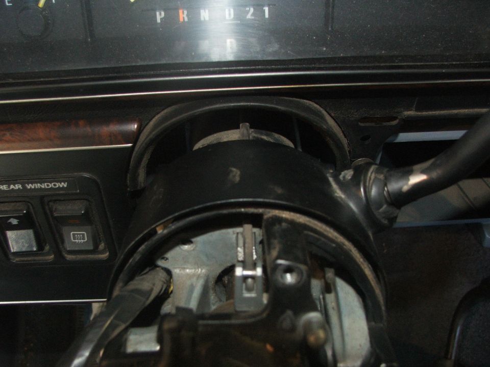 Interior view of a vehicle's steering column and dashboard, showing the gear selector and some buttons