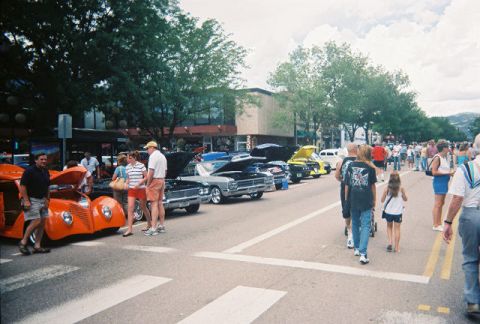 1972 Ford Ranchero - A street lined with classic cars and people attending a car show under a cloudy sky.