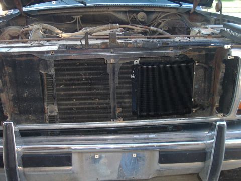 1982 Ford Bronco - The engine bay of an older truck displays a radiator and an added transmission cooler, with a chrome bumper below.