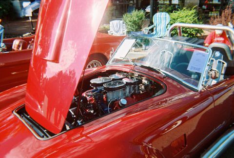 1972 Ford Ranchero - A red convertible displays its V8 engine at a car show, with another red vehicle partially visible behind it.