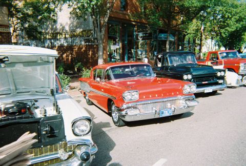 1972 Ford Ranchero - A red 1958 car is parked in front of a brick building, with other vehicles visible.
