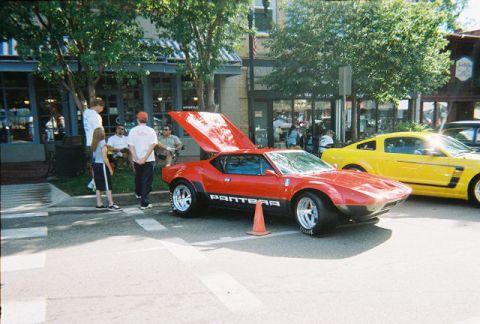 1972 Ford Ranchero - A red De Tomaso Pantera is displayed with its hood open, parked next to a yellow Ford Mustang at a car show.