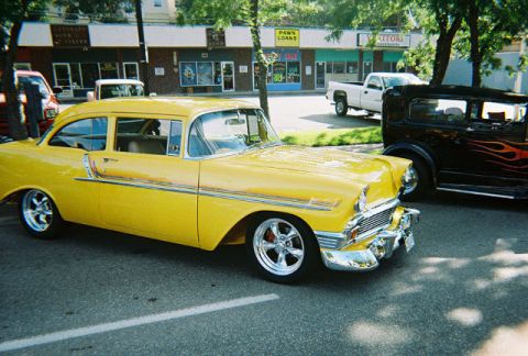 1972 Ford Ranchero - A bright yellow 1956 Chevrolet sedan is parked next to a black car with flames.