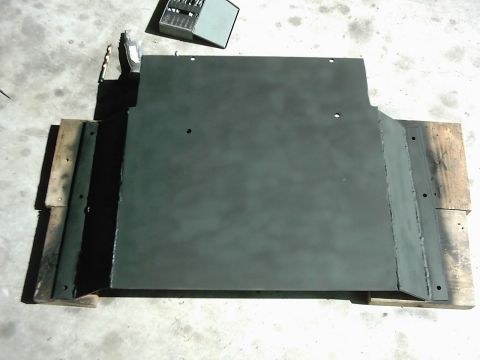 1978 Ford Bronco - A dark-colored metal skid plate rests on wooden planks, with tools visible in the background.