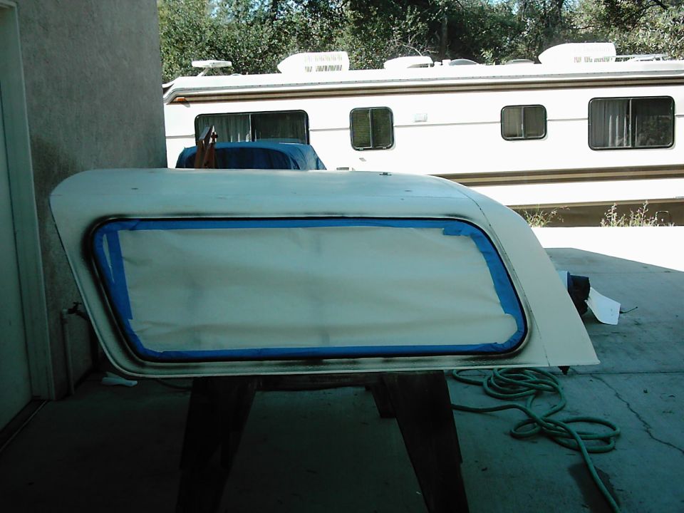 White car door with blue masking tape around the window frame, resting on sawhorses