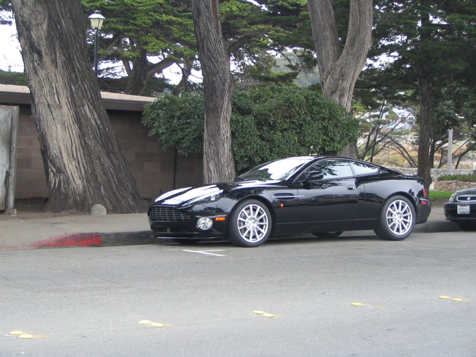 Black Aston Martin coupe parked on street, another car partially visible behind it