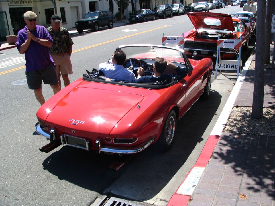 Red classic Ferrari convertible parked on a downtown street at a car show, rear 3/4 view