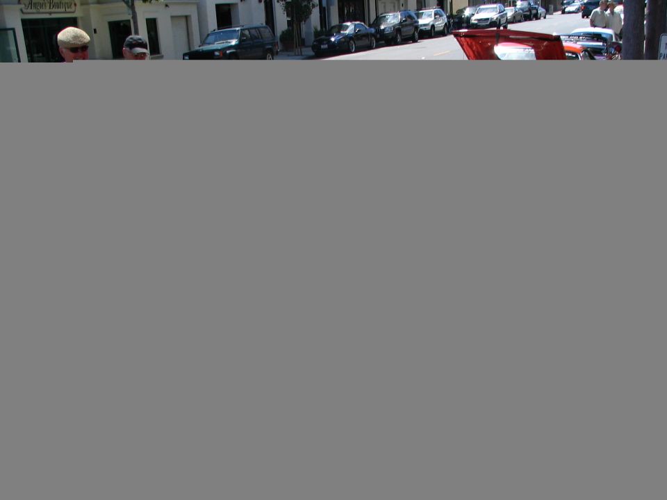 red convertible sports car parked on street, other cars and buildings in background
