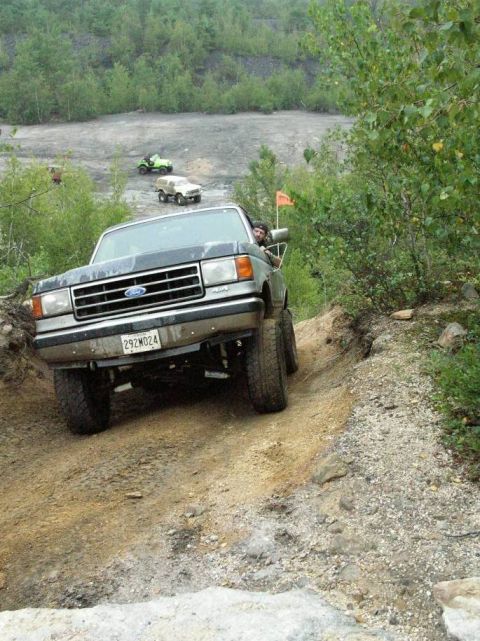 1995 Ford Bronco - Ford F-Series truck navigates a steep dirt trail with other off-road vehicles visible in the distance.