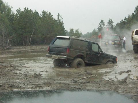 1995 Ford Bronco - Multiple SUVs navigate a muddy off-road course on an overcast day.
