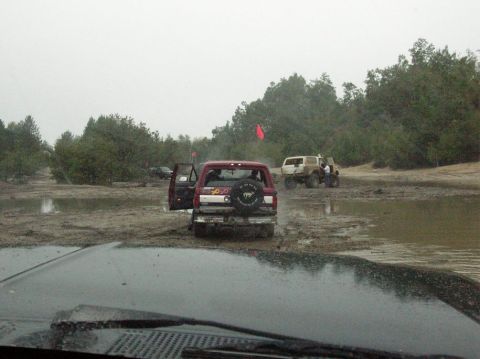 1995 Ford Bronco - Several off-road vehicles navigate a muddy terrain with trees in the background.