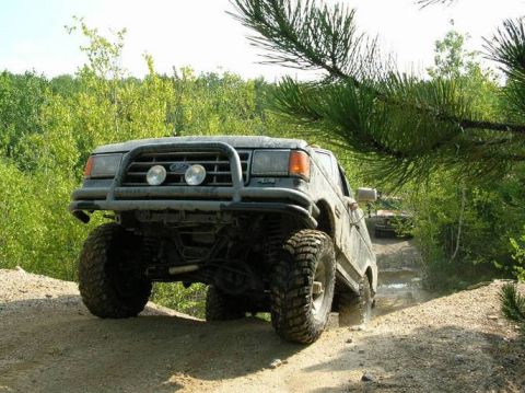 1995 Ford Bronco - This lifted SUV navigates a muddy trail, with another vehicle visible in the background.