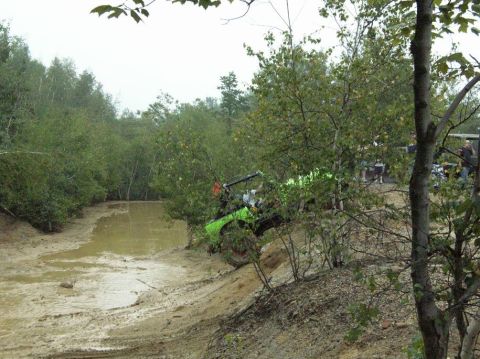 1995 Ford Bronco - Bright lime-green open-top 4x4 with an exposed roll cage nosing steeply down a sandy bank toward a muddy water pit, partly screened by brus…