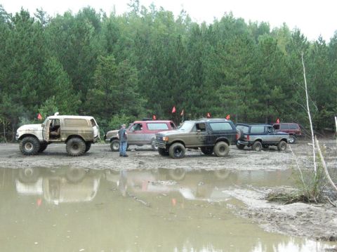 1995 Ford Bronco - Several off-road vehicles, including Ford Broncos, are gathered in a muddy area with trees in the background.