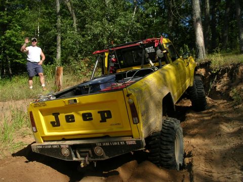 1977 Ford F-150 - A yellow Jeep pickup truck navigates a challenging off-road course with a man observing.