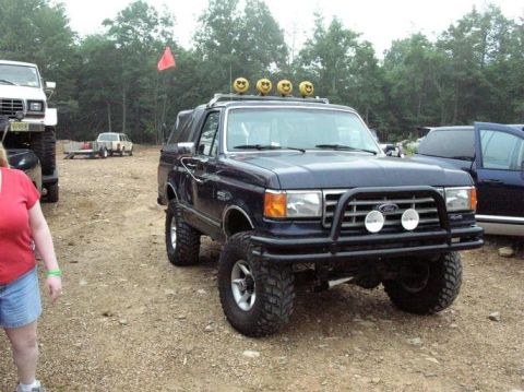 1995 Ford Bronco - This modified Ford Bronco, likely from the late 1980s, is parked outdoors with other vehicles.
