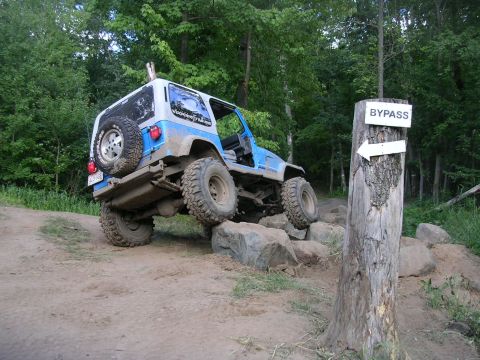 1977 Ford F-150 - A Jeep navigates a rocky obstacle on an off-road trail, with a bypass sign indicating an alternate route.