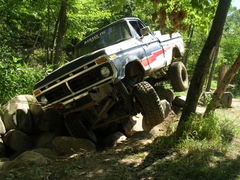 1977 Ford F-150 - A modified 1977 Ford F-150 navigates a challenging rocky obstacle course in a wooded area.