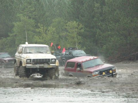 1995 Ford Bronco - Two lifted Ford Broncos work through a deep mud pit at an off-road park, a tan square-body on oversized mud tires and a red later model wit…