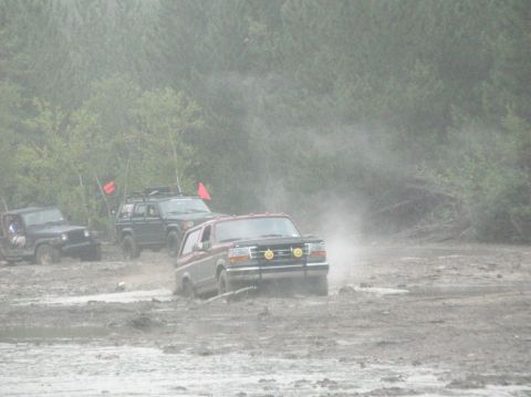 1995 Ford Bronco - A maroon Ford Bronco with a black brush guard and two yellow smiley-face light covers crosses a wide gray mud flat in drifting fog or steam…