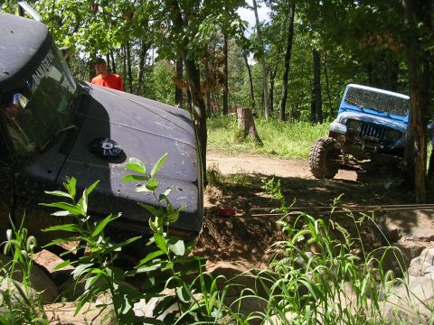 1977 Ford F-150 - Off-road vehicles tackle a challenging course in a wooded area, with one vehicle partially obscured by foliage.