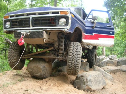1977 Ford F-150 - This modified pickup truck is navigating a challenging rocky terrain with its front wheel elevated.
