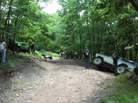 1995 Ford Bronco - A silver 1995 Ford Bronco is tilted on a dirt path, surrounded by trees and other off-road vehicles.