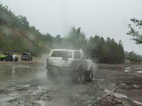 1995 Ford Bronco - Several off-road vehicles navigate a muddy terrain under an overcast sky.