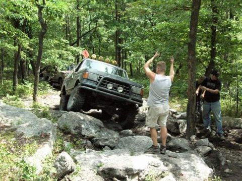 1995 Ford Bronco - A man gestures while a Ford Bronco tackles a challenging off-road course with other vehicles present.
