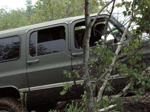 1995 Ford Bronco - A dark green SUV is seen from the side, with trees and foliage partially covering the vehicle.