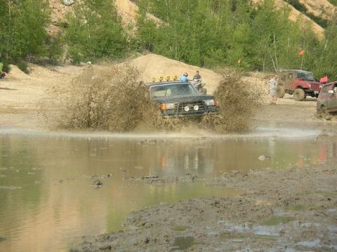 1995 Ford Bronco - Multiple off-road vehicles navigate a muddy terrain, creating large splashes.