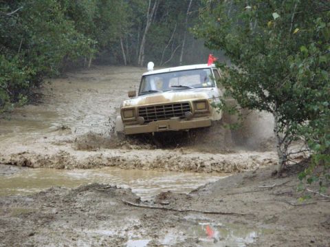 1995 Ford Bronco - Off-road vehicle navigates a muddy terrain, kicking up water and mud.