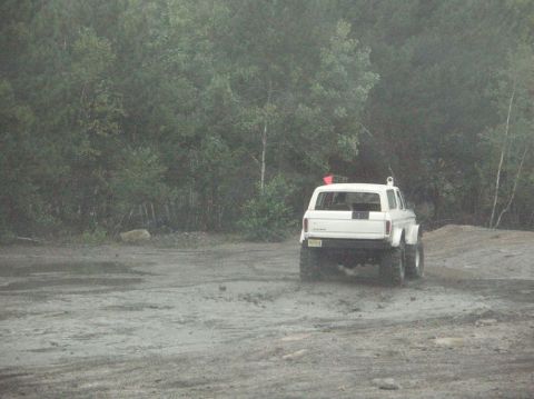 1995 Ford Bronco - A white SUV navigates a muddy terrain surrounded by trees, with a red flag visible on its roof.