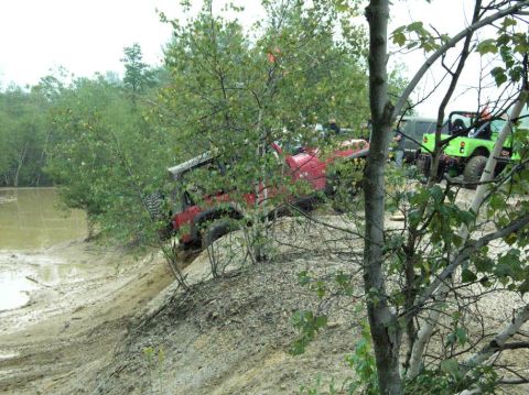 1995 Ford Bronco - Two off-road vehicles navigate a challenging muddy terrain with dense foliage.